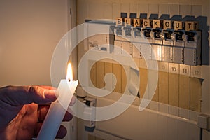 Fuse box with fuses in a distribution box during a power outage lit with white candle holding a man with the word blackout as text