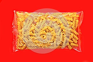 Fusili pasta in plastic package isolated on red background.