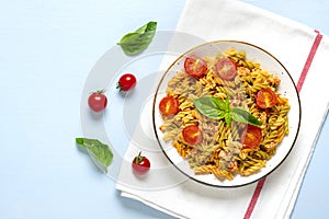 Fusilli - classic italian pasta from durum wheat with chicken meat, tomatoes cherry, basil in tomato sauce in white bowl on blue w