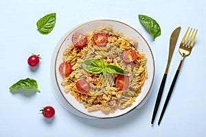 Fusilli - classic italian pasta from durum wheat with chicken meat, tomatoes cherry, basil in tomato sauce in white bowl, napkin,