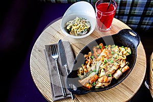 Fusilli pasta with chicken and vegetables in a black pan on a wooden table