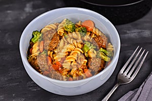 Fusilli pasta, meatballs, broccoli and carrot vegetable bowl and on dark table