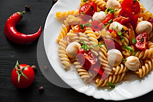pasta salad with tomato, pepper and mozzarella balls in plate on dark wooden background