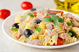 Fusilli pasta salad with tuna, tomatoes, black olives and basil on gray stone background