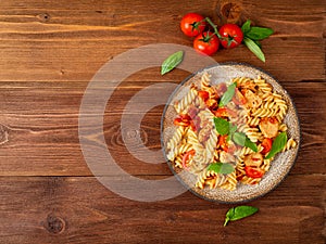 Fusilli pasta with tomato sauce, chicken fillet with basil leaves on dark brown wooden background, copy space, top view