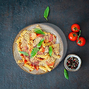 Fusilli pasta with tomato sauce, chicken fillet with basil leaves on dark stone concrete background, top view