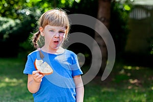 Fussy eater, little girl, picky child eating a slice of bread with butter displeased, choosy kid behavior, doesn`t want to eat