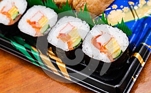 Futomaki, appetizing sushi roll with cucumber, salmon, egg, imitation crab stick and seaweed. Serving on black plastic plate from