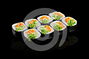Futomaki rolls with salmon, tobiko and greens on black background