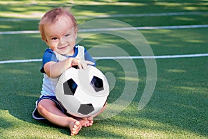 Future football star: Smiling infant with a soccer ball. Happy little boy at football field playing with ball