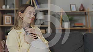 Future mother holding ultrasound scan while sitting on sofa