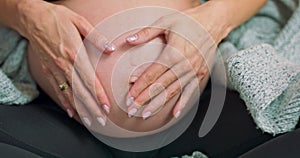 Future mother petting abdomen and showing heart shape. Close up of woman pregnant belly. Concept