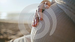 Future mother stroking tummy on sunset beach closeup. Woman hand caressing belly