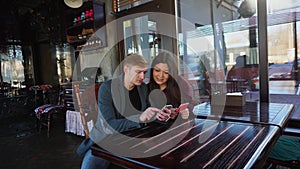 Future parents choosing clothes for child in coffee house with smartphones