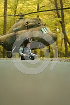 Future pilot. Kid sitting at helicopter on natural background