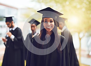 The future starts today. a happy young graduate standing outside with fellow students in the background.