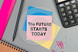 The future starts today - text on sticky note. Top view image of pink card, pencil, calculator and with many paper clips on table
