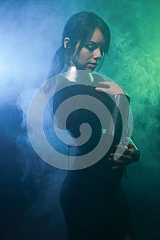Futuristic fashion model wearing black and silver clothes and standing in the colorful blue and green smoke
