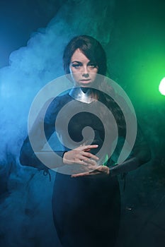 Futuristic fashion model wearing black and silver clothes and standing in the colorful blue and green smoke