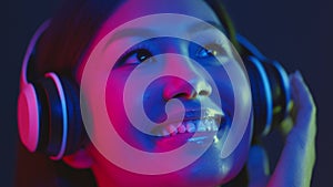 Futuristic music concept. Young happy asian woman enjoying music with wireless headphones, smiling in bright neon lights