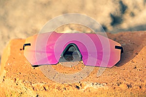 Futuristic sunglasses model rimless with big pink lens reflecting the sun in a summer day closeup. Selective focus