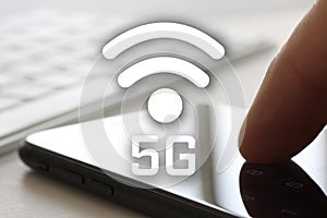 5G network concept with finger touching smartphone with screen and keybord in background. Wireless internet symbol in front of dis photo