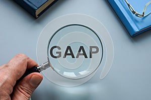 GAAP Generally Accepted Accounting Principles. A hand with a magnifying glass points to an abbreviation.