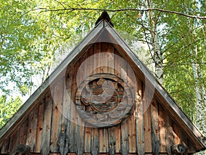 Gable old wooden house on the background of birches and blue sky