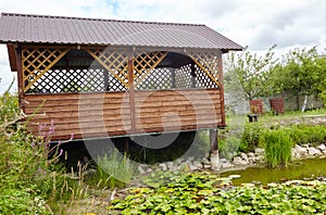 A gable roof gazebo near decorative pond on backyard on a sunny day