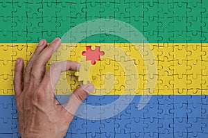 Gabon flag is depicted on a puzzle, which the man`s hand completes to fold