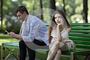 Gadget addiction. Bored young girl and her boyfriend stuck in cellphone on dull date at park photo