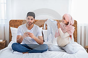 Gadget addiction concept. Careless muslim husband using smartphone, ignoring his pregnant wife