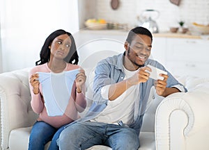 Gadget addiction concept. Egoistic black man playing games on cellphone, neglecting his expectant wife at home