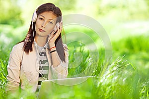 Gadget freak concept. Portrait of fashionable hipster girl in pink leather jacket listening to music on pc, sitting in green grass