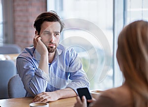 Gadget overuse concept. Bored young guy having dull date, his girlfriend stuck in smartphone at city cafe