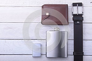 Gadgets and accessories for men on light wooden background. Fashionable men s belt, wallet, lighter, Stainless hip flask