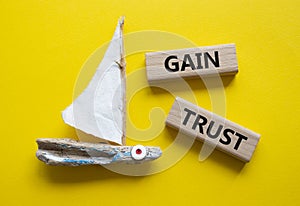 Gain trust symbol. Wooden blocks with words Gain trust. Beautiful yellow background with boat. Business and Gain trust concept.