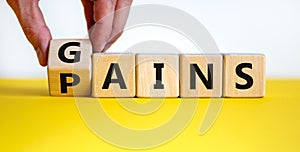 Gains and pains symbol. Businessman turns wooden cubes, changes word pains to gains. Beautiful yellow table, white background.