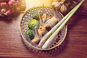 Galangal, lemongrass, kaffir lime, shallot, garlic in basket on wooden background, fresh herbs and spices or ingredients healthy