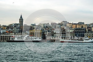 Galata Tower, on its hill, in Karakoy and Beyoglu district, taken during a cloudy winter afternoon, while the sea, ferry boats