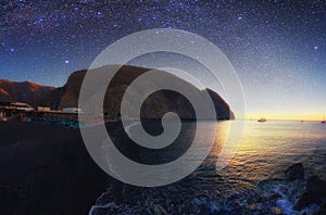 Galaxy over  Perissa beach with Black volcano sand of at summer sunset.