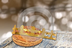 Galette des rois, french kingcake with a golden crown, on wooden table ,epiphany cake against blury light
