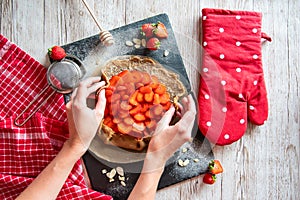 Galette with strawberries preparation, detail of hands of cooker. Pie cake placed on black desk and wooden table with cooking