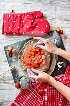 Galette with strawberries preparation, detail of hands of cooker. Pie cake placed on black desk and wooden table with cooking