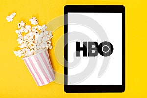 Popcorn bucket and tablet with HBO logo on yellow background. Top view