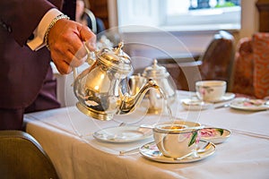 Gallant waiter pouring the tea, traditional English afternoon tea ceremony