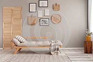 Posters in black frames and wicker kinck knack on beige wall of trendy living room interior with long settee with photo