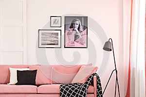 Gallery of posters on empty white wall of bright living room interior with pink settee photo