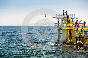 Galway city, Ireland - 24.04.2021: Girl and a woman jumping off Blackrock diving board into Atlantic ocean water. high tide, Clear