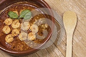 Gambas al pilpil or Prawns pil pil in clay dish with wooden spoon
